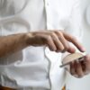 Nahaufnahme einer Person in weißem Hemd, die mit dem Finger auf ein Smartphone tippt – Symbol für mobile Interaktion und digitale Kommunikation