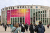Besucher betreten Messe Berlin zur DMEA-Konferenz – großes Banner mit ‚Time to connect Digital Health‘ an der Gebäudefassade weist auf Veranstaltung zur digitalen Gesundheit hin