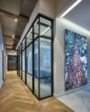 Moderner Büroflur mit Glas-Meetingräumen und Naturfotografie – stilvolle Arbeitsumgebung mit Holzfußboden und Lichtdesign