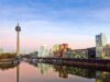 Panorama des Düsseldorfer Medienhafens mit modernen Bürogebäuden, dem Rheinturm und Spiegelung der Skyline im Wasser bei Sonnenuntergang.