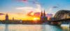 Blick auf den Rhein in Köln mit Dom, Hohenzollernbrücke und Stadtansicht bei Sonnenuntergang.