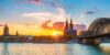Blick auf den Rhein in Köln mit Dom, Hohenzollernbrücke und Stadtansicht bei Sonnenuntergang.
