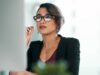 Berufliche Arbeitssituation: Person mit Brille am Schreibtisch, konzentrierter Blick in modernem Büro